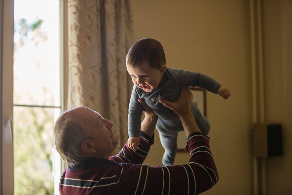 man wearing maroon, white, and blue stripe long-sleeved shirt lifting up baby wearing gray onesie